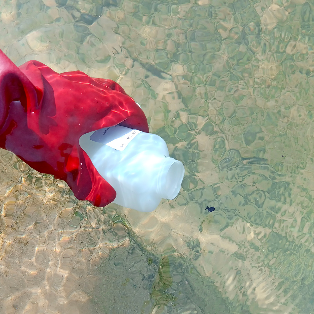 photo d'une main gantée tenant une bouteille pour faire un prélévement qualité dans une riviere