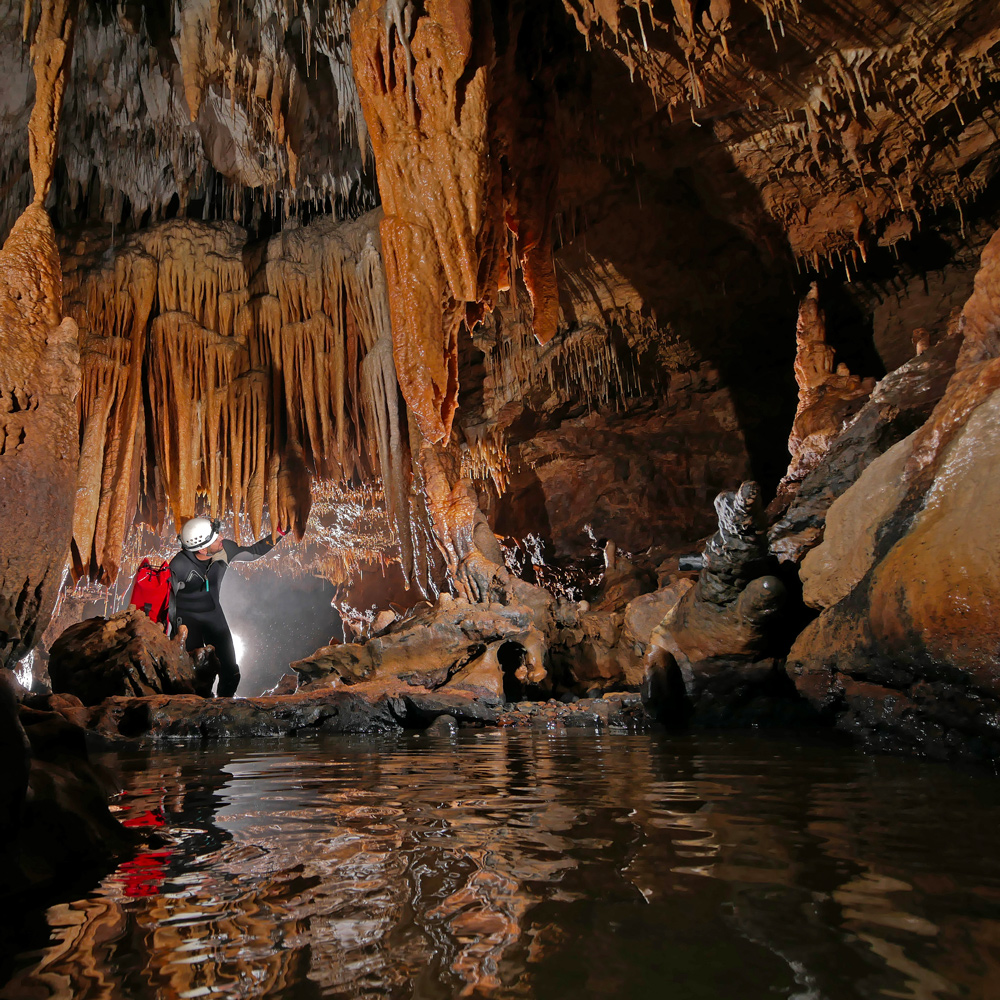 Photo d'un cours d'eau souterrain, dans une grotte avec de nombreux stalactites et en présence d'un spéléologue